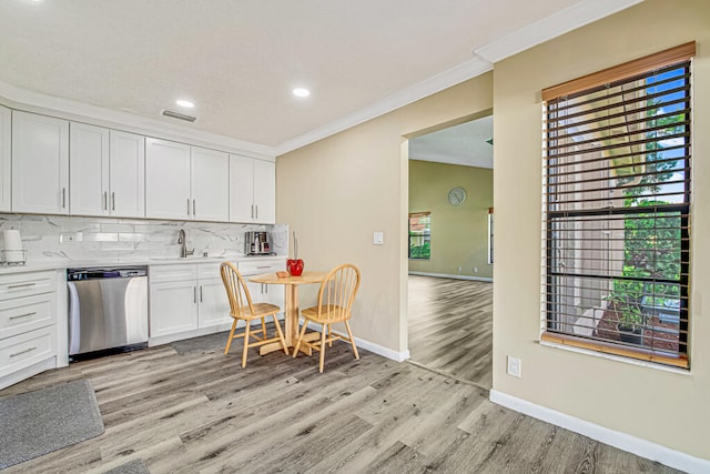 kitchen featuring white cabinets, decorative backsplash, ornamental molding, stainless steel dishwasher, and light hardwood / wood-style flooring