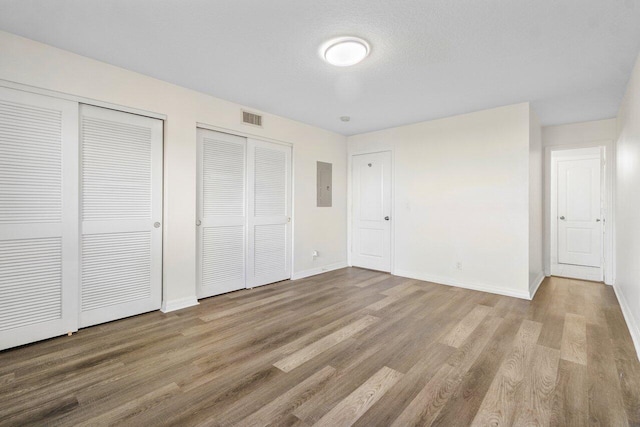 unfurnished bedroom featuring multiple closets, light wood-type flooring, a textured ceiling, and electric panel