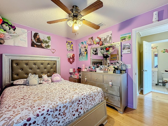 bedroom featuring ceiling fan, ensuite bathroom, light wood-type flooring, and a textured ceiling