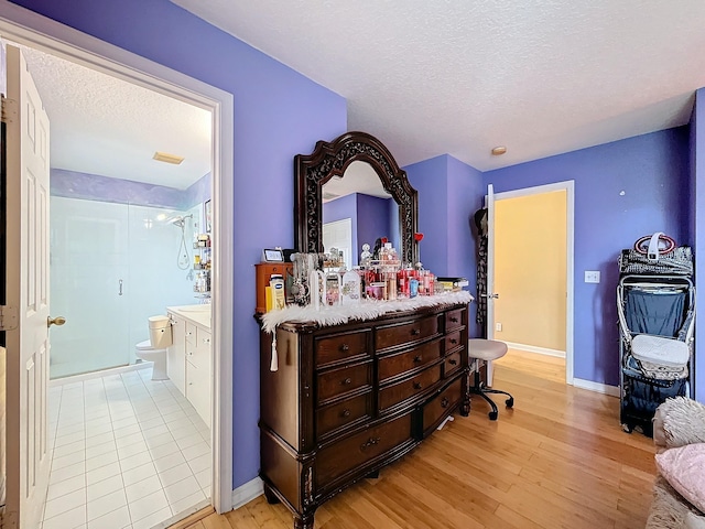 bedroom with ensuite bath, light hardwood / wood-style flooring, and a textured ceiling