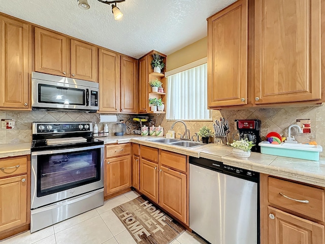 kitchen with tile countertops, sink, a textured ceiling, appliances with stainless steel finishes, and light tile patterned flooring