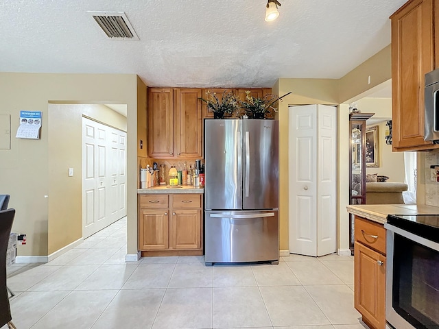 kitchen featuring appliances with stainless steel finishes, a textured ceiling, and light tile patterned floors