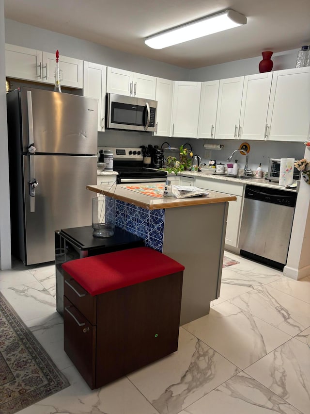 kitchen featuring white cabinetry, appliances with stainless steel finishes, light tile patterned flooring, a center island, and sink