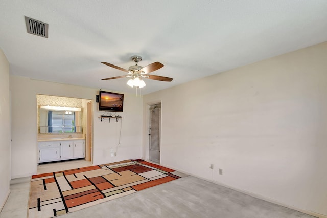 unfurnished bedroom featuring ceiling fan, light carpet, and ensuite bath