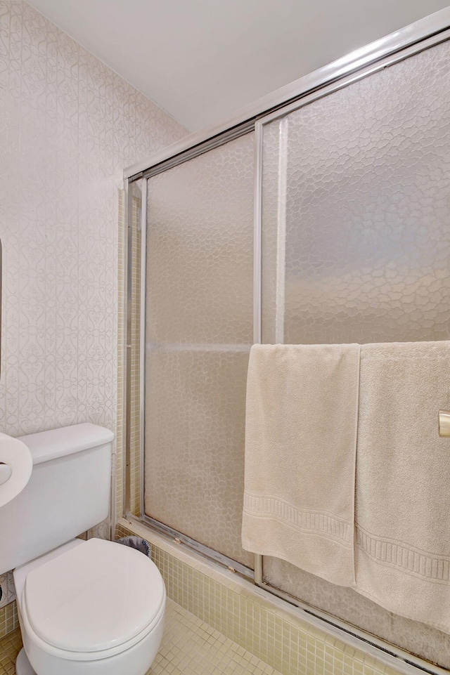 bathroom featuring toilet, a shower with door, and tile patterned flooring