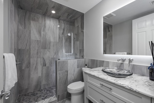 bathroom with vanity, tiled shower, tile walls, and toilet