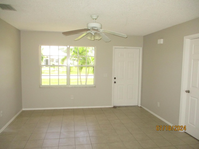 empty room with a textured ceiling, light tile patterned floors, and ceiling fan