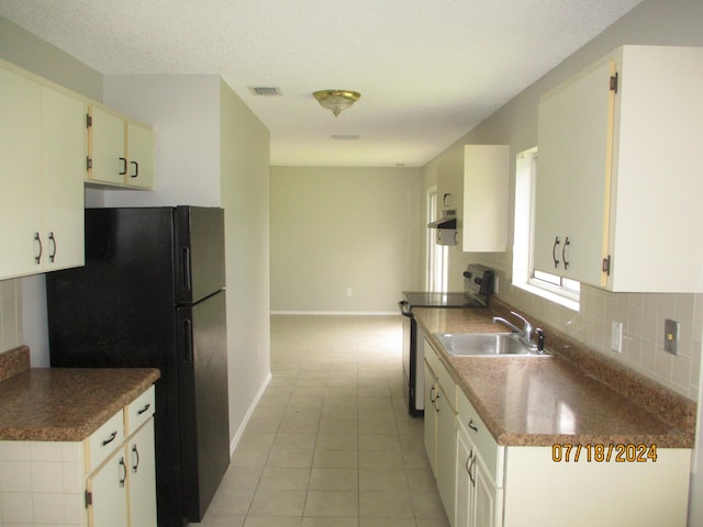 kitchen featuring white cabinets, black refrigerator, tasteful backsplash, and light tile patterned floors