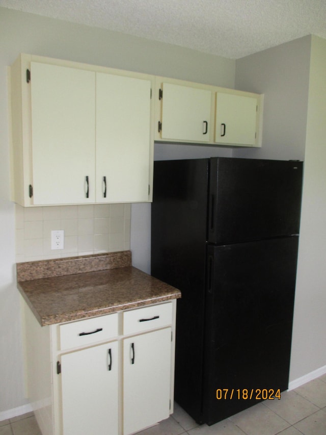 kitchen with white cabinetry, tasteful backsplash, light tile patterned floors, a textured ceiling, and black refrigerator