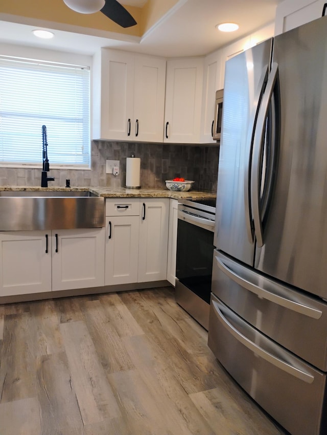 kitchen with appliances with stainless steel finishes, white cabinets, sink, light hardwood / wood-style floors, and decorative backsplash