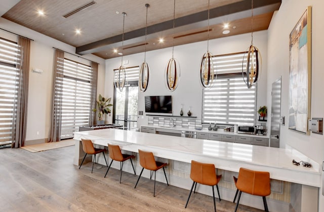 kitchen with light hardwood / wood-style floors, beamed ceiling, hanging light fixtures, and a kitchen breakfast bar