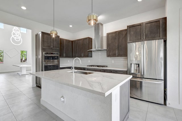 kitchen featuring hanging light fixtures, wall chimney exhaust hood, appliances with stainless steel finishes, sink, and a center island with sink