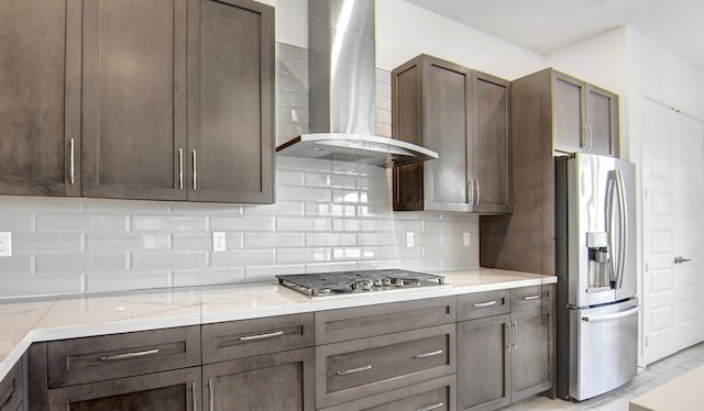 kitchen featuring wall chimney range hood, stainless steel appliances, decorative backsplash, light stone countertops, and light tile patterned floors