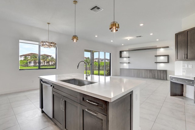 kitchen with a center island with sink, sink, hanging light fixtures, light tile patterned floors, and stainless steel dishwasher