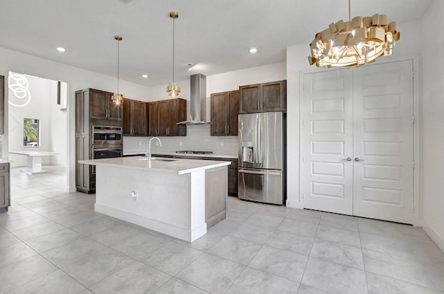 kitchen featuring an island with sink, wall chimney exhaust hood, appliances with stainless steel finishes, decorative light fixtures, and sink