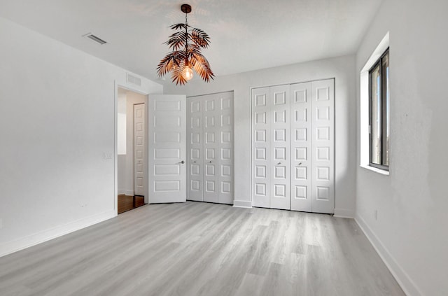 unfurnished bedroom featuring two closets and light wood-type flooring