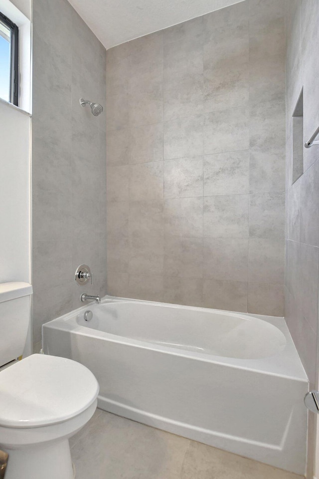 bathroom with tiled shower / bath combo, toilet, and tile patterned floors