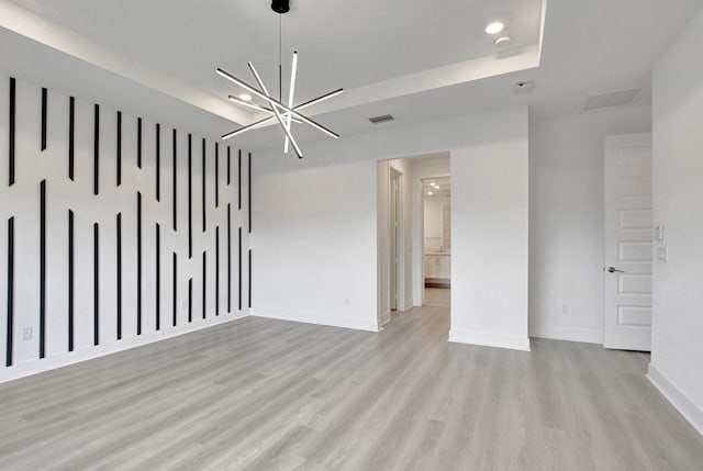 unfurnished room featuring an inviting chandelier, light wood-type flooring, and a raised ceiling