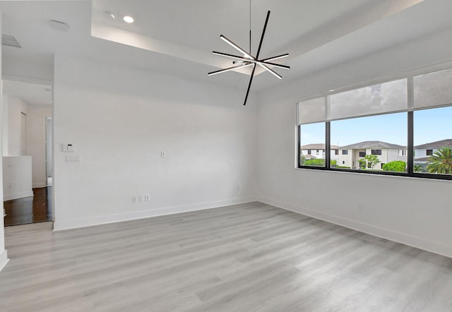 spare room featuring a raised ceiling, light wood-type flooring, and a chandelier