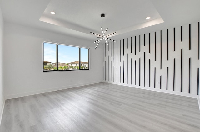 spare room with an inviting chandelier, light wood-type flooring, and a tray ceiling