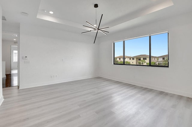 spare room with light hardwood / wood-style flooring, a healthy amount of sunlight, a chandelier, and a tray ceiling