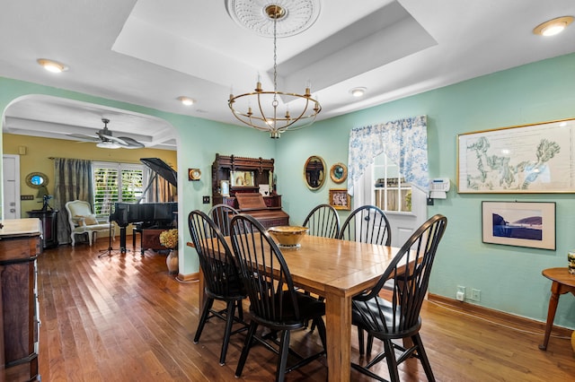 dining room with ceiling fan with notable chandelier, a raised ceiling, and hardwood / wood-style floors