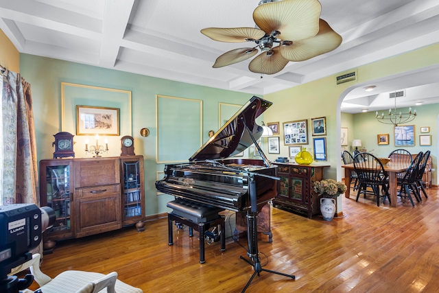 miscellaneous room with ceiling fan with notable chandelier, beamed ceiling, hardwood / wood-style flooring, and coffered ceiling