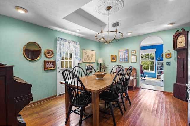 dining area featuring wood-type flooring, a textured ceiling, a raised ceiling, and an inviting chandelier