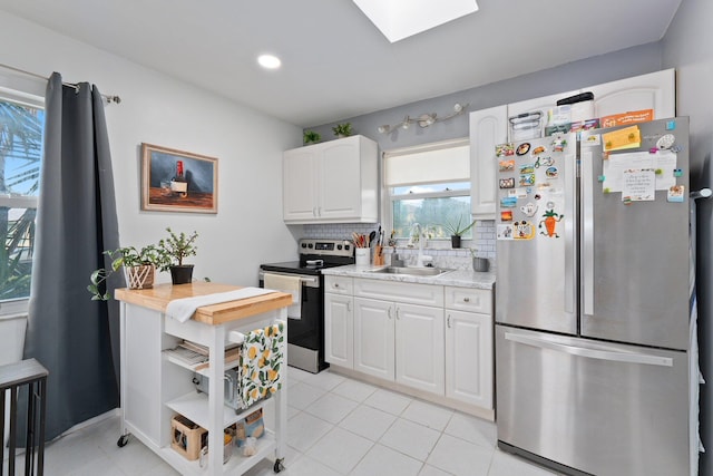 kitchen with appliances with stainless steel finishes, a skylight, tasteful backsplash, sink, and white cabinets