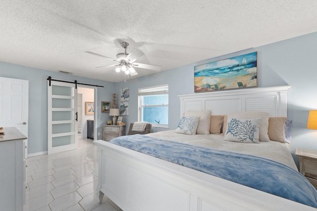 bedroom featuring light tile patterned flooring, a barn door, ceiling fan, and a textured ceiling