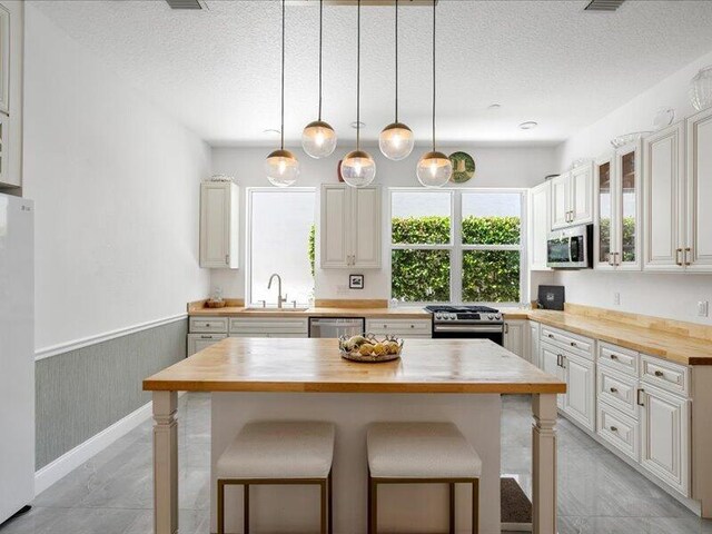 kitchen with a kitchen bar, appliances with stainless steel finishes, wooden counters, a textured ceiling, and a center island