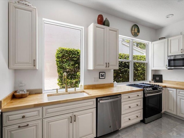 kitchen with sink, light tile patterned floors, wooden counters, and stainless steel appliances