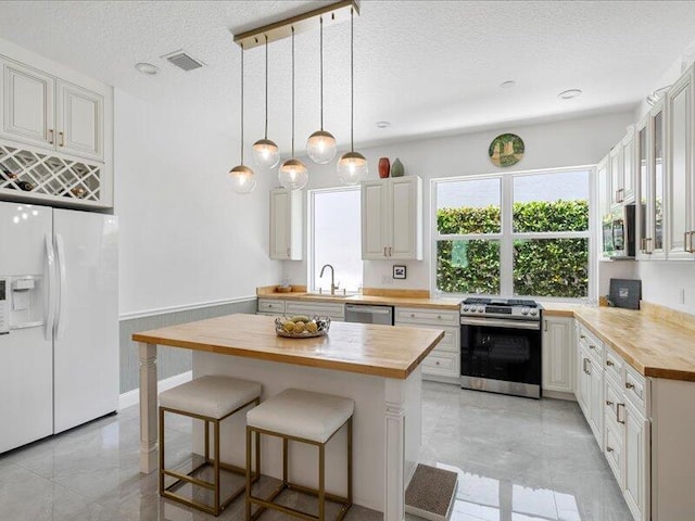 kitchen featuring light tile patterned flooring, hanging light fixtures, appliances with stainless steel finishes, a textured ceiling, and wood counters