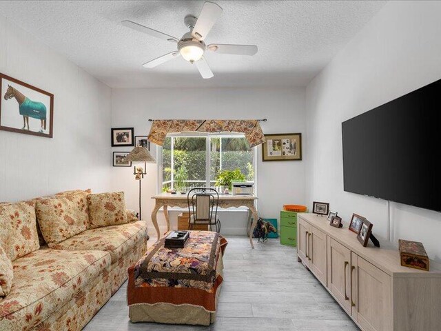 living room featuring light hardwood / wood-style flooring, a textured ceiling, and ceiling fan