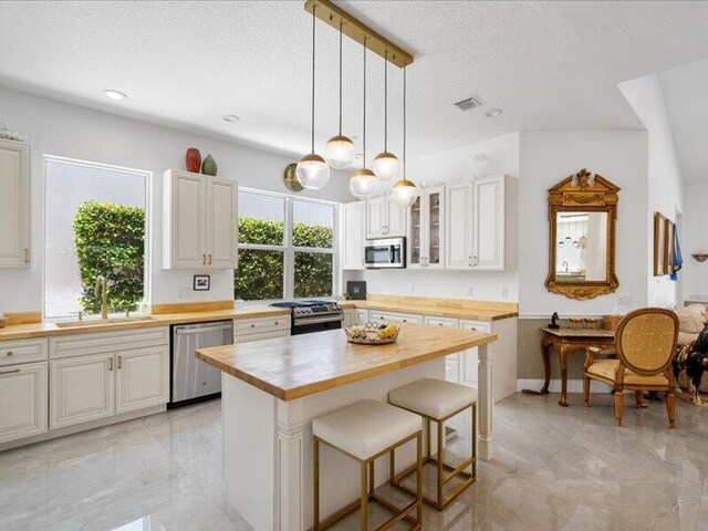 kitchen featuring light tile patterned floors, a kitchen bar, stainless steel appliances, decorative light fixtures, and sink