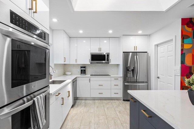 kitchen featuring white cabinetry, stainless steel appliances, sink, light stone counters, and backsplash