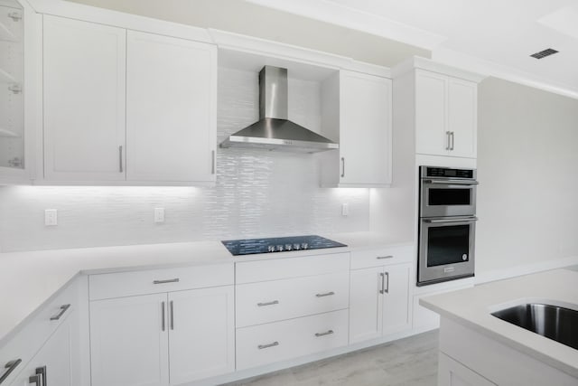 kitchen featuring decorative backsplash, white cabinetry, stainless steel double oven, and wall chimney exhaust hood