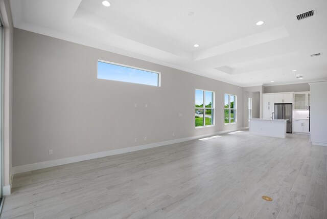 unfurnished living room with light hardwood / wood-style floors, a raised ceiling, and ornamental molding