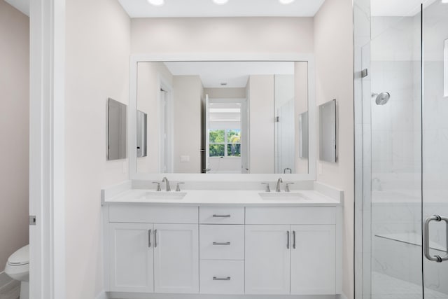 bathroom featuring a shower with shower door, toilet, and dual bowl vanity