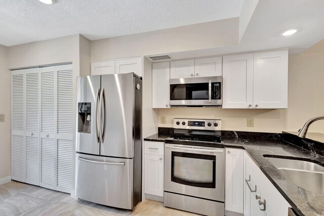 kitchen with sink, white cabinetry, dark stone counters, and stainless steel appliances