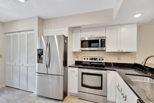 kitchen with appliances with stainless steel finishes, sink, white cabinetry, dark stone counters, and a textured ceiling