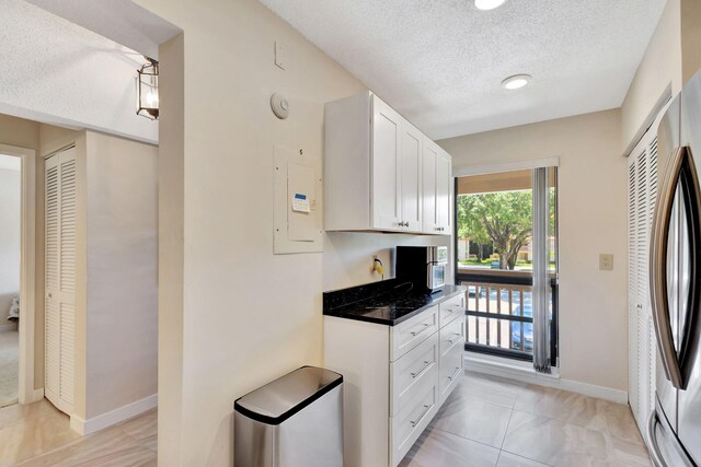 kitchen with light tile patterned flooring, stainless steel refrigerator, a textured ceiling, white cabinets, and electric panel