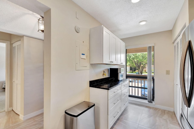 kitchen with fridge, white cabinets, light tile patterned floors, a textured ceiling, and dark stone countertops