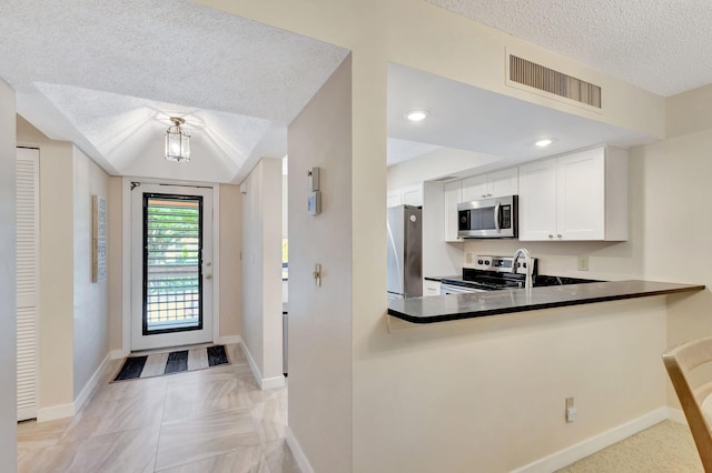 kitchen with white cabinets, kitchen peninsula, appliances with stainless steel finishes, and a textured ceiling