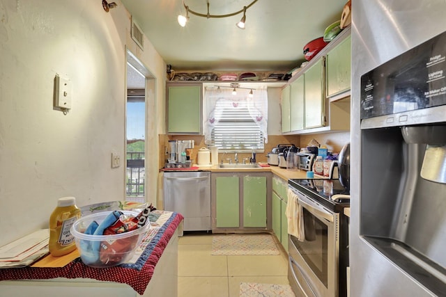 kitchen with sink, green cabinetry, light tile patterned floors, and stainless steel appliances