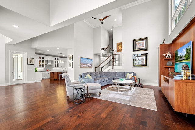 living room with crown molding, ceiling fan, dark hardwood / wood-style floors, and a towering ceiling