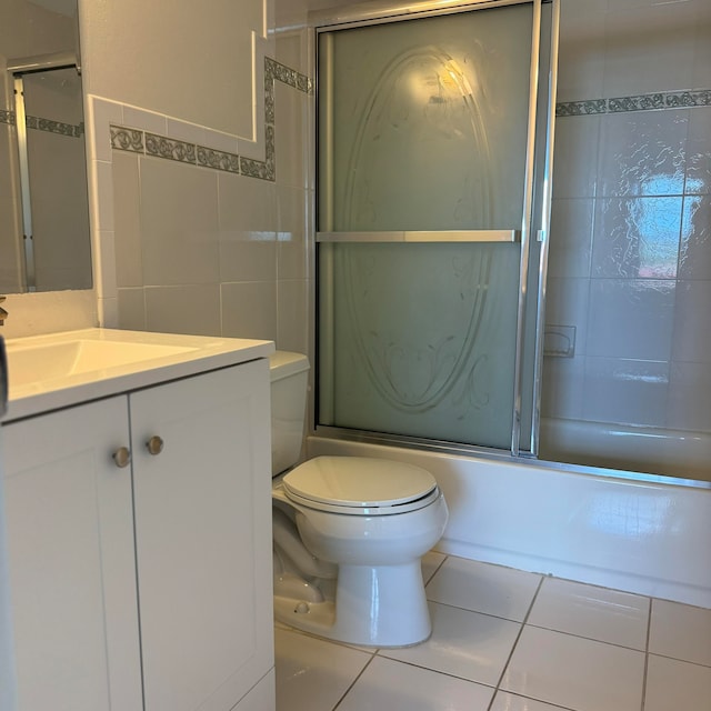 full bathroom featuring combined bath / shower with glass door, tile walls, vanity, tile patterned floors, and toilet