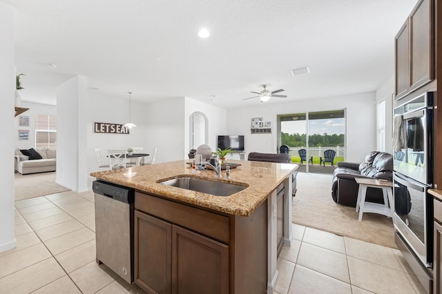 kitchen with sink, appliances with stainless steel finishes, light stone countertops, an island with sink, and decorative light fixtures