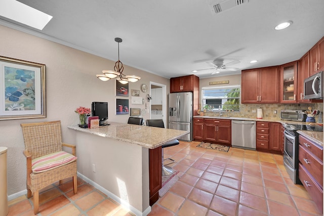 kitchen with appliances with stainless steel finishes, kitchen peninsula, a skylight, light tile patterned flooring, and ceiling fan