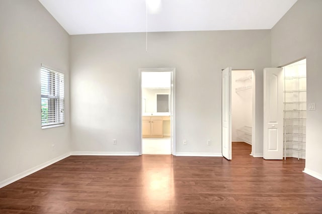 unfurnished bedroom featuring connected bathroom, a spacious closet, dark wood-type flooring, and a closet